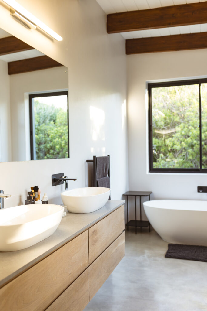Renovated modern bathroom featuring a floating wood vanity with vessel sinks, a freestanding tub, and large windows bringing in natural light.
