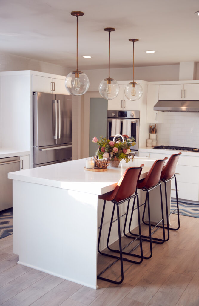 Bright modern kitchen with white cabinets, a large island with barstools, stainless steel appliances, and pendant lighting.