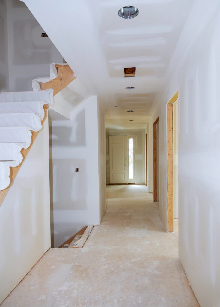 Interior hallway under renovation with newly installed drywall, unfinished flooring, and staircase preparation in a residential home.
