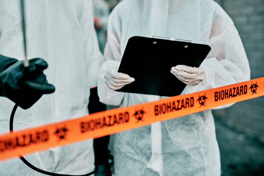 Technicians in protective suits evaluating biohazard and environmental hazards in a home behind biohazard tape.